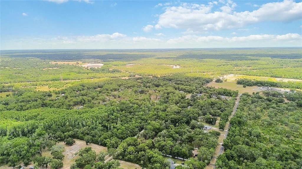 An aerial view shows a rural landscape with dense trees, scattered houses, and open fields — 5018 N ANDRI DRIVE, CRYSTAL RIVER, FL