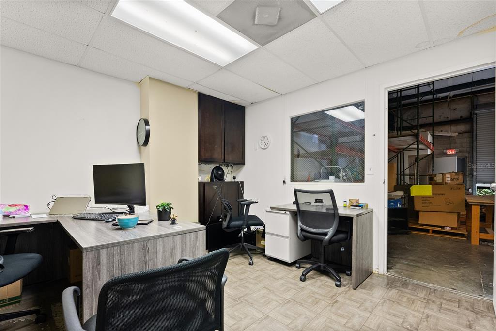 An office space features two desks, rolling chairs, dark cabinetry, and a window overlooking a warehouse — 1410-1430 TROPIC PARK DRIVE UNIT 1410-1430, SANFORD, FL
