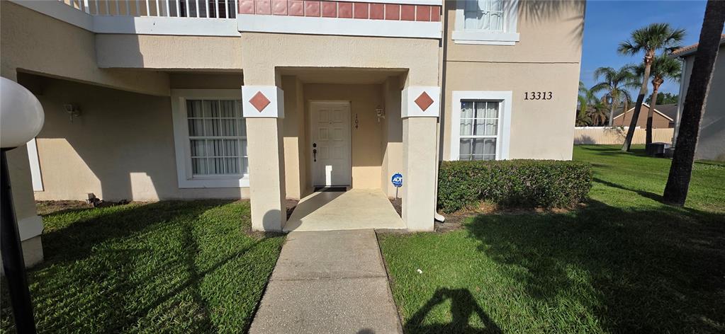 The exterior of a beige two-story residential building features a covered entryway and a sidewalk — 13313 FAIRWAY GLEN DRIVE UNIT 104, ORLANDO, FL