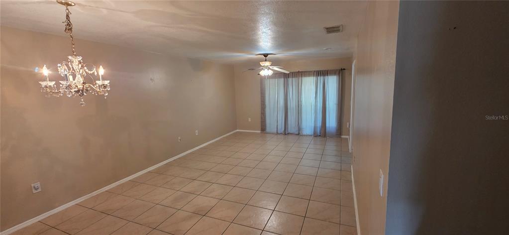 A spacious room features light-colored tile flooring, a crystal chandelier, and sliding glass doors — 13313 FAIRWAY GLEN DRIVE UNIT 104, ORLANDO, FL