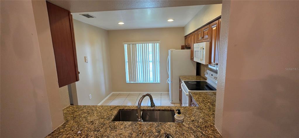 A kitchen features granite countertops, wood cabinets, a white refrigerator, and a dining area — 13313 FAIRWAY GLEN DRIVE UNIT 104, ORLANDO, FL