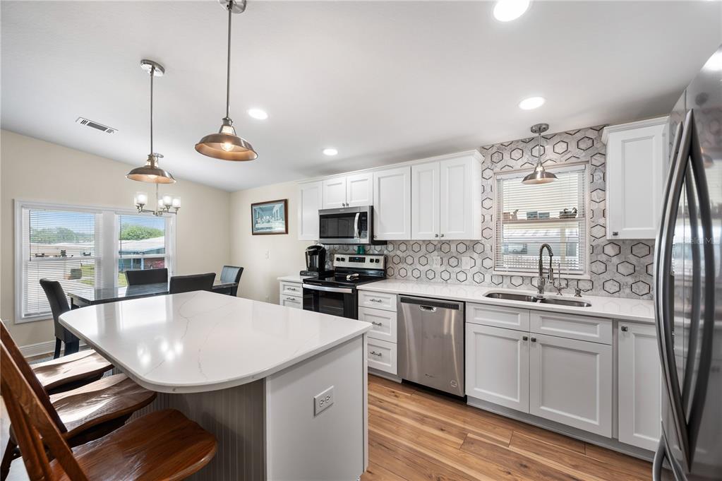 A kitchen features white cabinets, a quartz island, stainless steel appliances, and a hexagonal backsplash — 1502 LONGBOW DRIVE, LAKELAND, FL