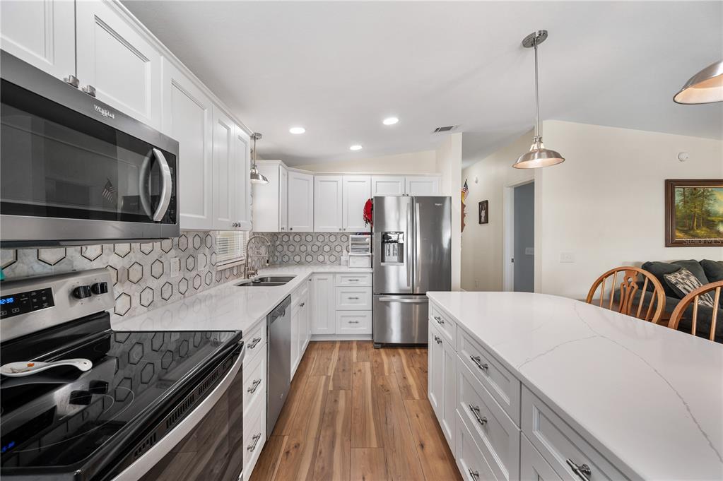A modern kitchen features white cabinets, stainless steel appliances, quartz countertops, and wood-look flooring — 1502 LONGBOW DRIVE, LAKELAND, FL