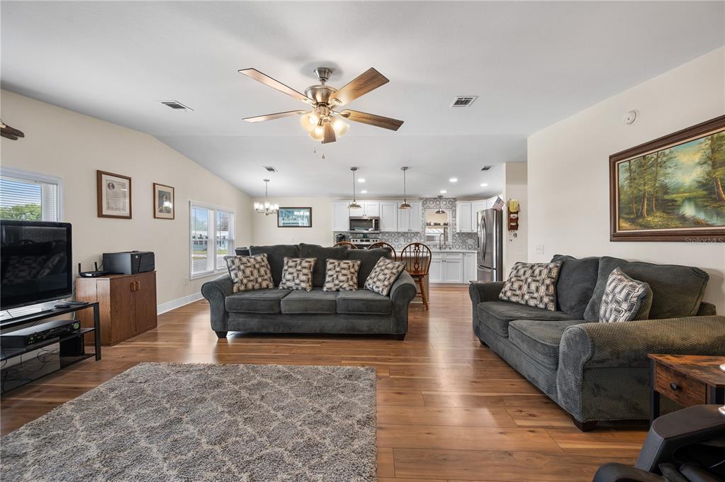 A living room with hardwood floors, two gray sofas, and an open kitchen in the background — 1502 LONGBOW DRIVE, LAKELAND, FL