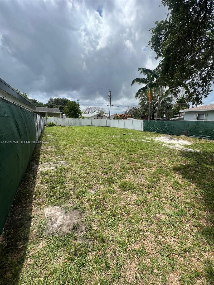 A vacant, grassy residential lot is enclosed by a white fence and green privacy screens — 6122 Garfield St, Hollywood FL 33024, HOLLYWOOD, FL