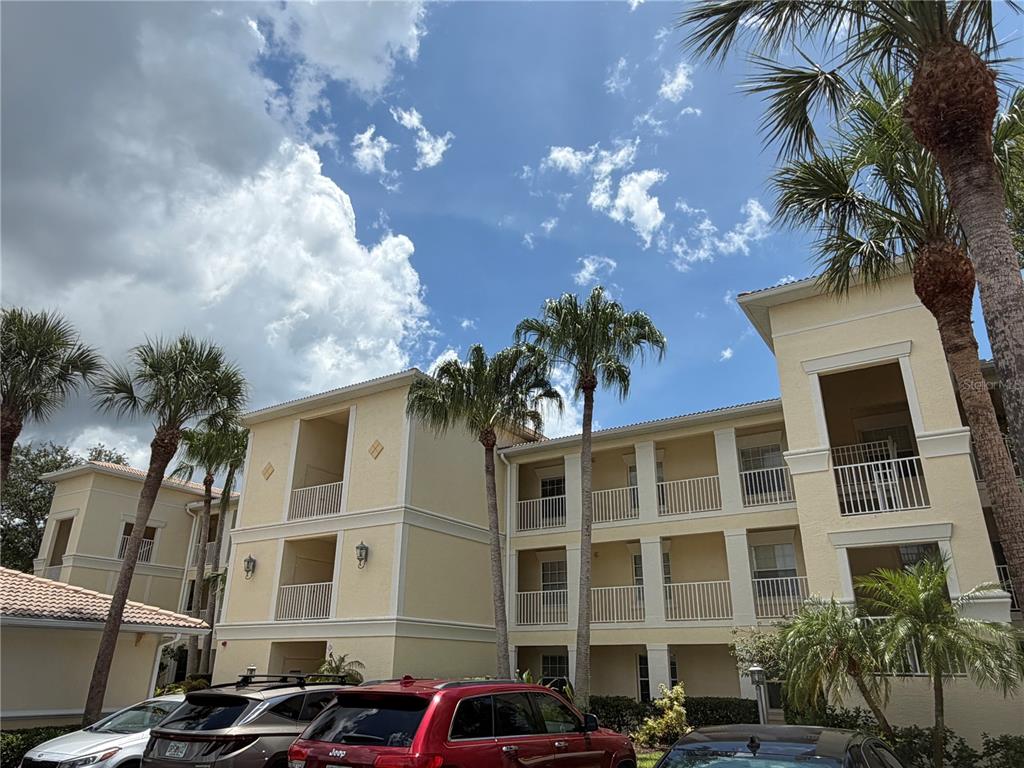A three-story apartment building with beige stucco walls and palm trees under a cloudy sky — 600 GARDENS EDGE DRIVE UNIT 633, VENICE, FL