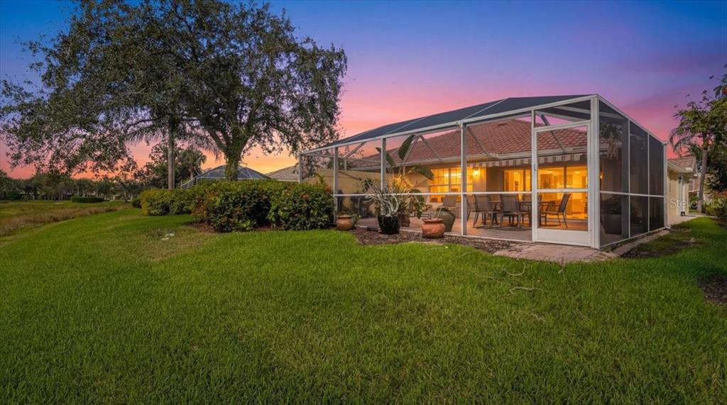 A screened-in patio with outdoor furniture sits behind a house next to a grassy lawn — 5546 MODENA PLACE, SARASOTA, FL