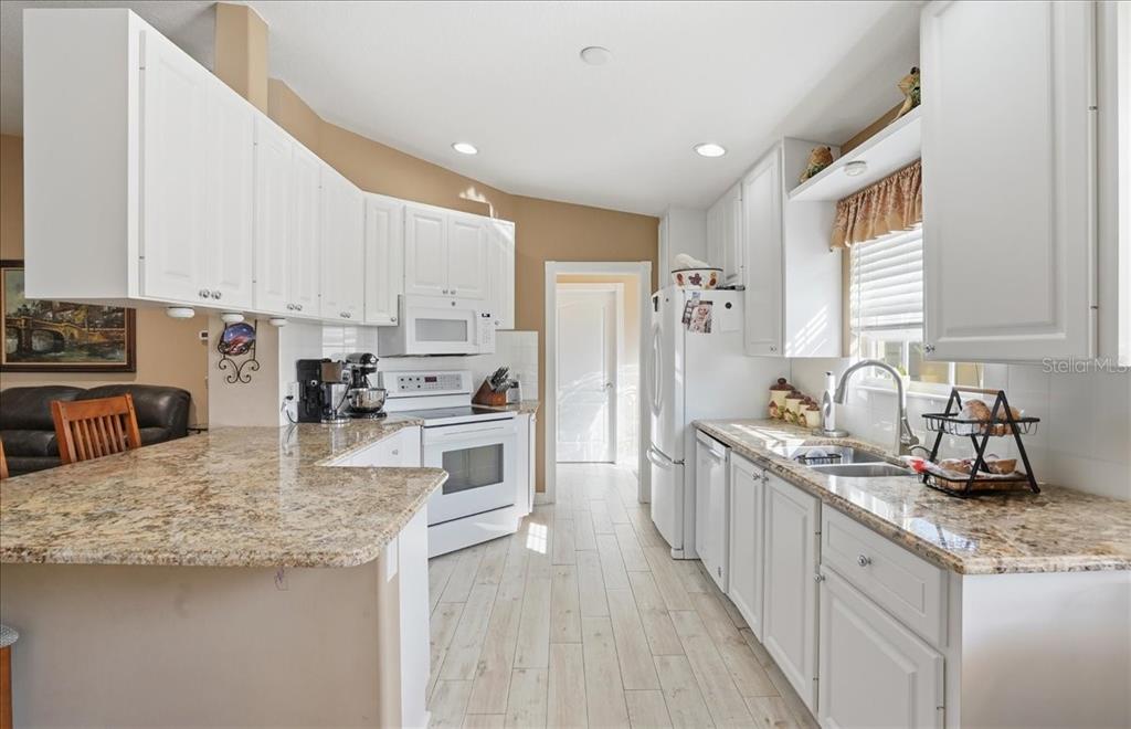 A kitchen features white cabinets, granite countertops, white appliances, and light wood-look tile flooring — 5546 MODENA PLACE, SARASOTA, FL