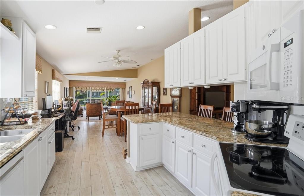 A kitchen with white cabinets and granite countertops opens into a dining and living area — 5546 MODENA PLACE, SARASOTA, FL