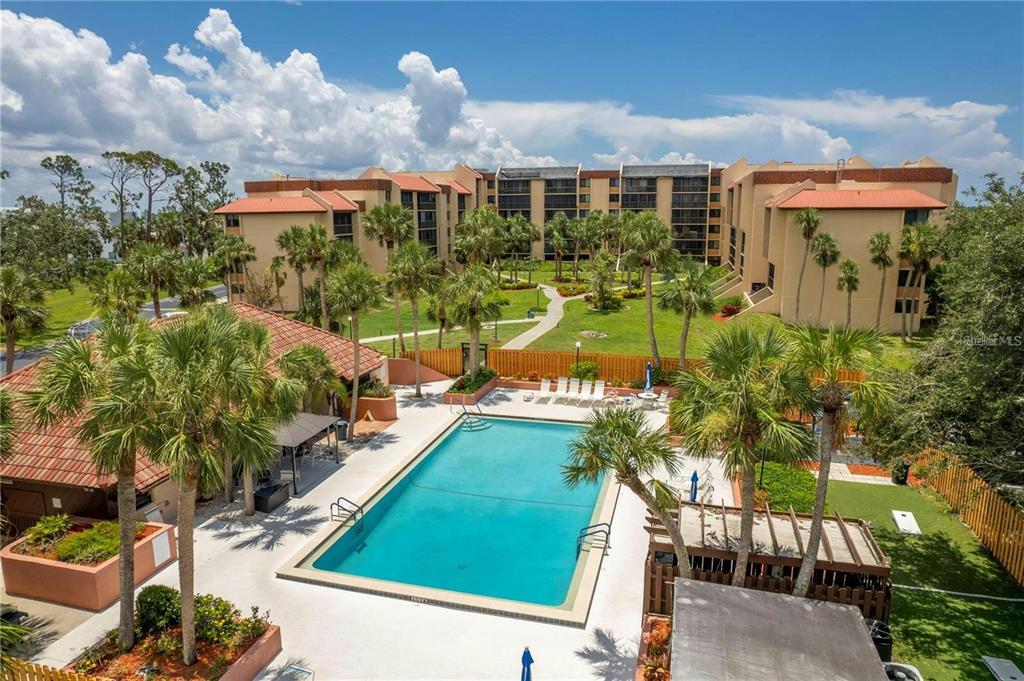 An aerial view of a swimming pool surrounded by palm trees and a multi-story apartment building — 3006 CARING WAY UNIT 409, PORT CHARLOTTE, FL