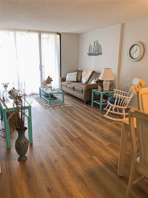 A living room features wood-look flooring, a brown sofa, a rocking chair, and teal tables — 3006 CARING WAY UNIT 409, PORT CHARLOTTE, FL