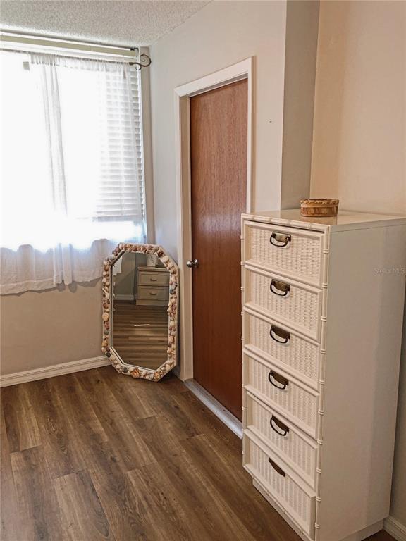 A bedroom features wood-look flooring, a white wicker dresser, a seashell-framed mirror, and a window — 3006 CARING WAY UNIT 409, PORT CHARLOTTE, FL