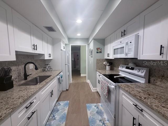 A galley kitchen features white cabinets, granite countertops, and stainless steel appliances — 143 WHISPERING SANDS DRIVE UNIT N/A, SARASOTA, FL
