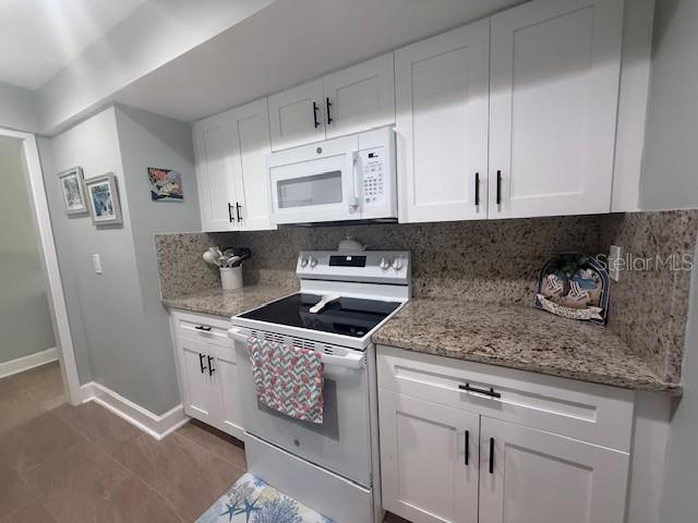 A kitchen features white cabinets, granite countertops, and white appliances against light blue walls — 143 WHISPERING SANDS DRIVE UNIT N/A, SARASOTA, FL