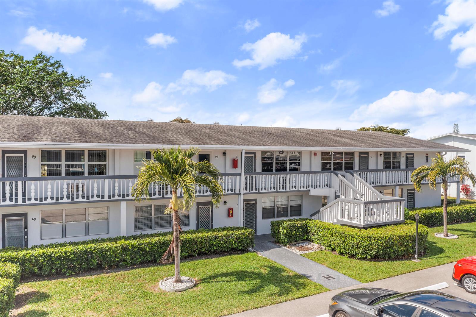 A two-story apartment building with a white exterior, balconies, and a palm tree in front — 97 Oakridge H # 97, Deerfield Beach FL 33442, DEERFIELD BEACH, FL