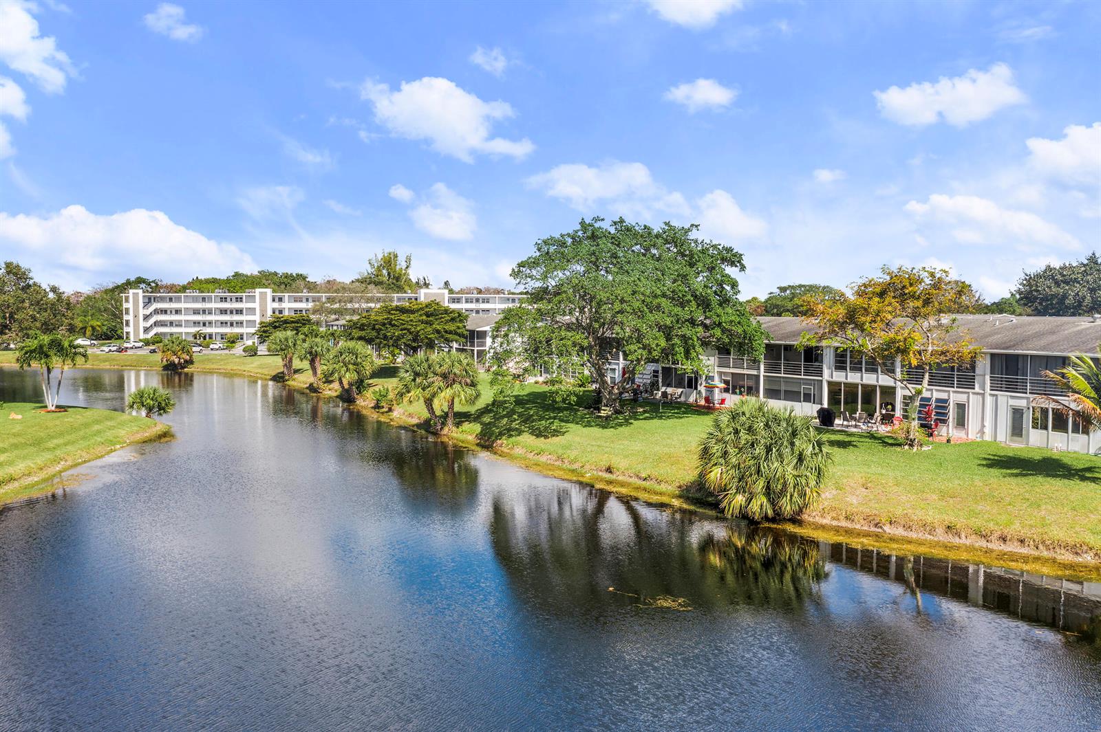 An exterior view of apartment buildings situated along a calm canal with surrounding palm trees — 97 Oakridge H # 97, Deerfield Beach FL 33442, DEERFIELD BEACH, FL