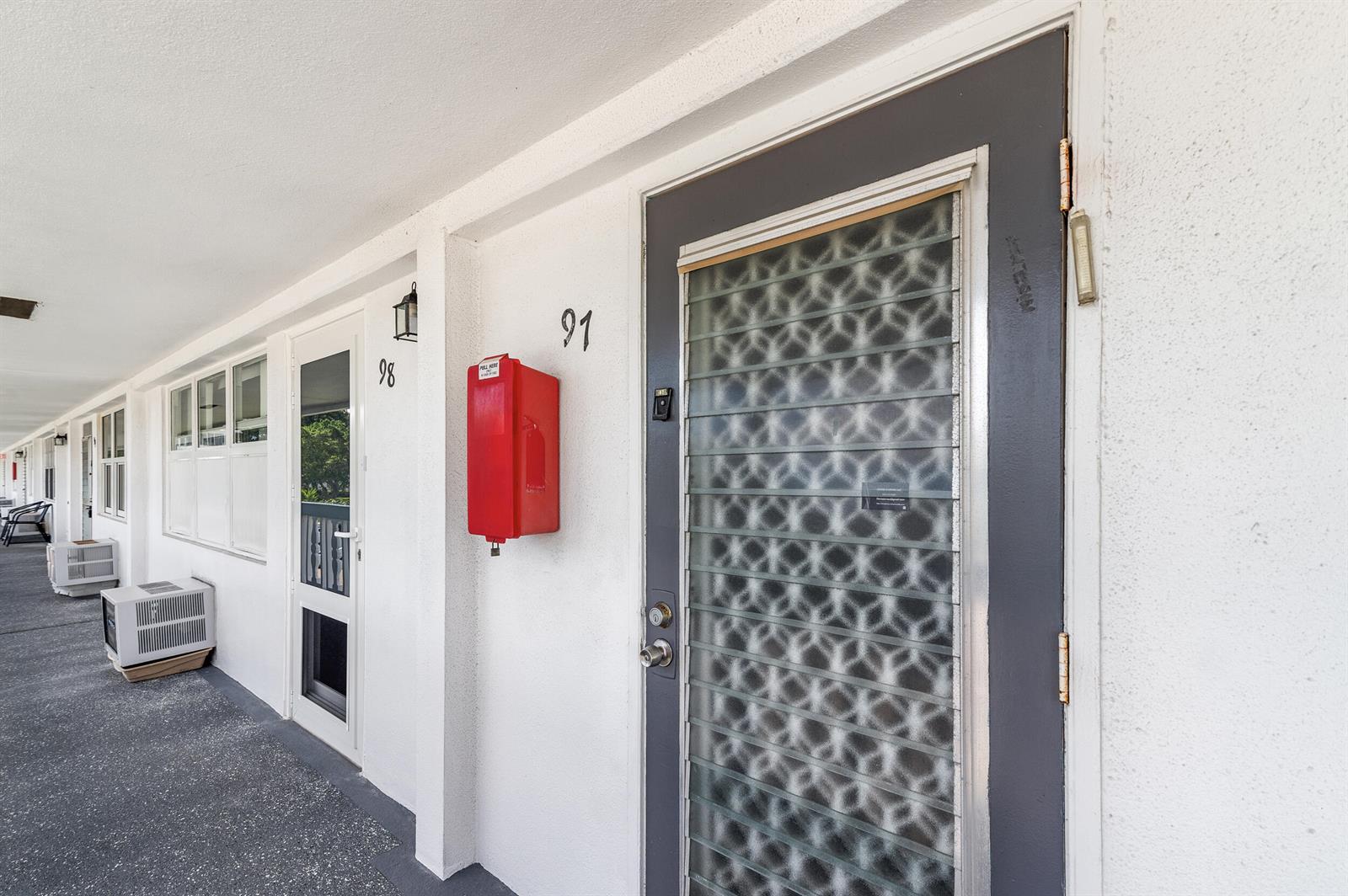 An exterior walkway shows apartment doors numbered 91 and 98 with a red fire alarm box — 97 Oakridge H # 97, Deerfield Beach FL 33442, DEERFIELD BEACH, FL