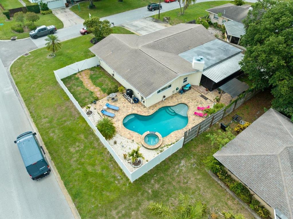 An aerial view shows a house with a backyard pool, spa, and white privacy fence — 1560 BEL KEENE DRIVE, CLEARWATER, FL