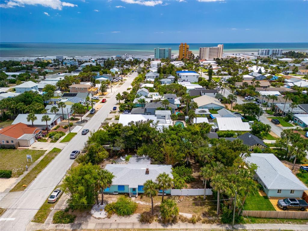An aerial view shows a light blue house surrounded by trees near a coastal beach — 705 N PENINSULA AVENUE, NEW SMYRNA BEACH, FL