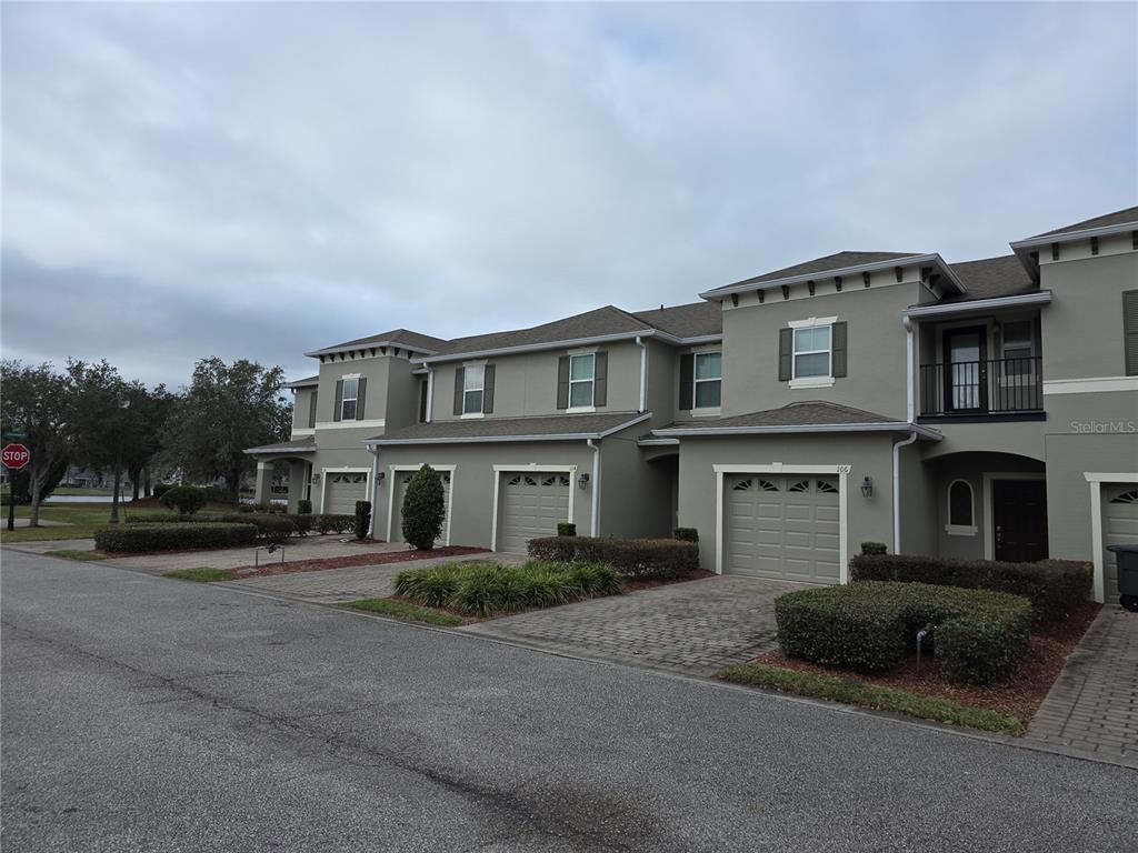 A row of multi-story townhomes with beige stucco exteriors, attached garages, and paved driveways — 104 KELLY THOMAS WAY, DAYTONA BEACH, FL