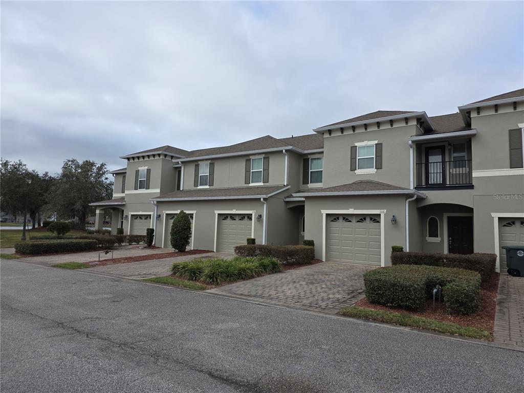 A row of two-story townhomes with beige stucco siding, attached garages, and paved driveways — 104 KELLY THOMAS WAY, DAYTONA BEACH, FL