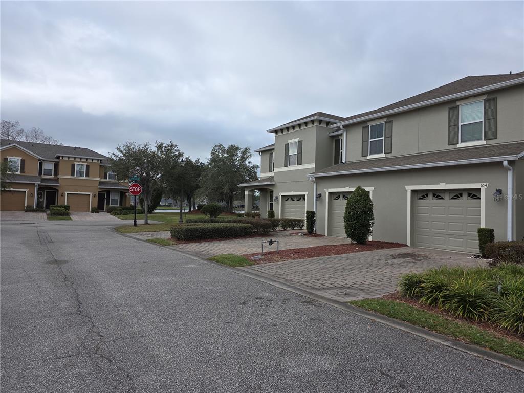 A street view of two-story townhomes with attached garages and paved driveways under a cloudy sky — 104 KELLY THOMAS WAY, DAYTONA BEACH, FL