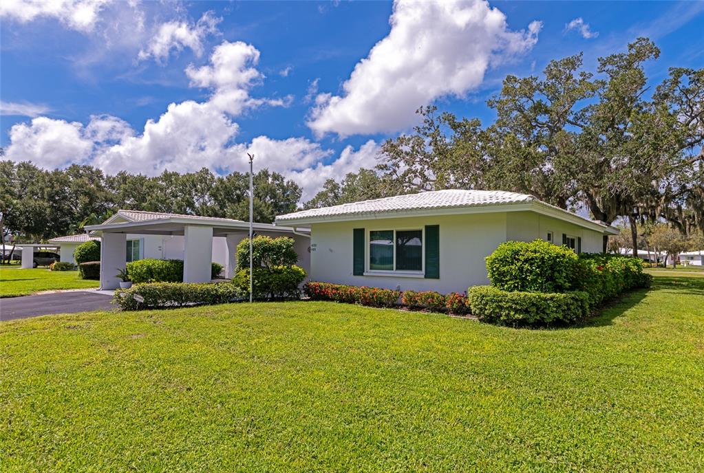 A single-story house with a white exterior, green shutters, and a carport under a blue sky — 4202 SCHWALBE DRIVE UNIT 89, SARASOTA, FL