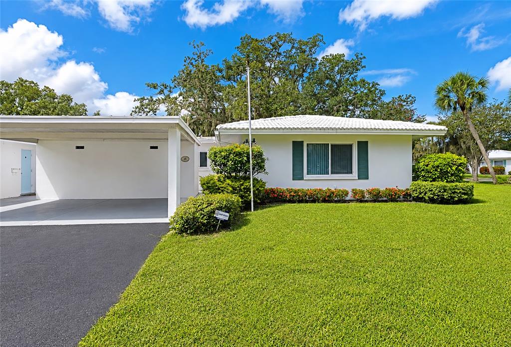 A white single-story house features a carport, green shutters, and a manicured lawn — 4202 SCHWALBE DRIVE UNIT 89, SARASOTA, FL