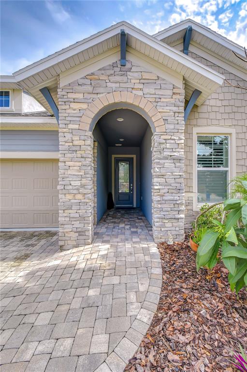 A stone-arched entryway leads to a front door with a paved walkway and shingled siding — 14014 SWALLOW HILL DRIVE, LITHIA, FL
