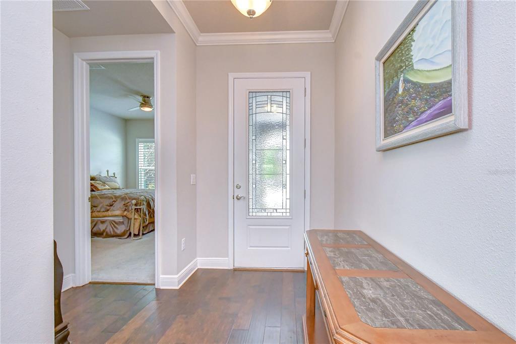 A foyer with dark wood flooring, a white front door, and a view into a bedroom — 14014 SWALLOW HILL DRIVE, LITHIA, FL