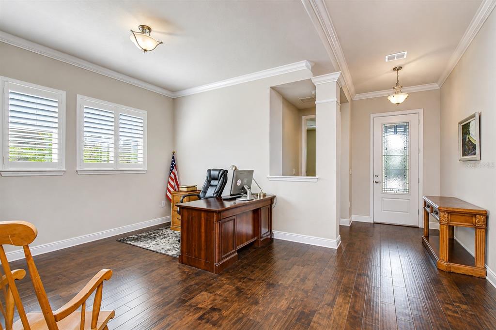 A home office features dark wood flooring, a wooden desk, and a front entryway door — 14014 SWALLOW HILL DRIVE, LITHIA, FL