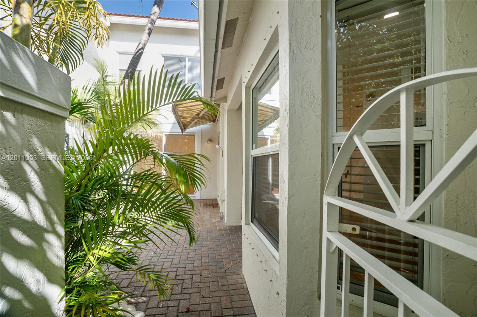 A brick-paved courtyard sits between a white stucco building and a decorative metal gate — 1640 Weeping Willow Way # 1640, Hollywood FL 33019, HOLLYWOOD, FL
