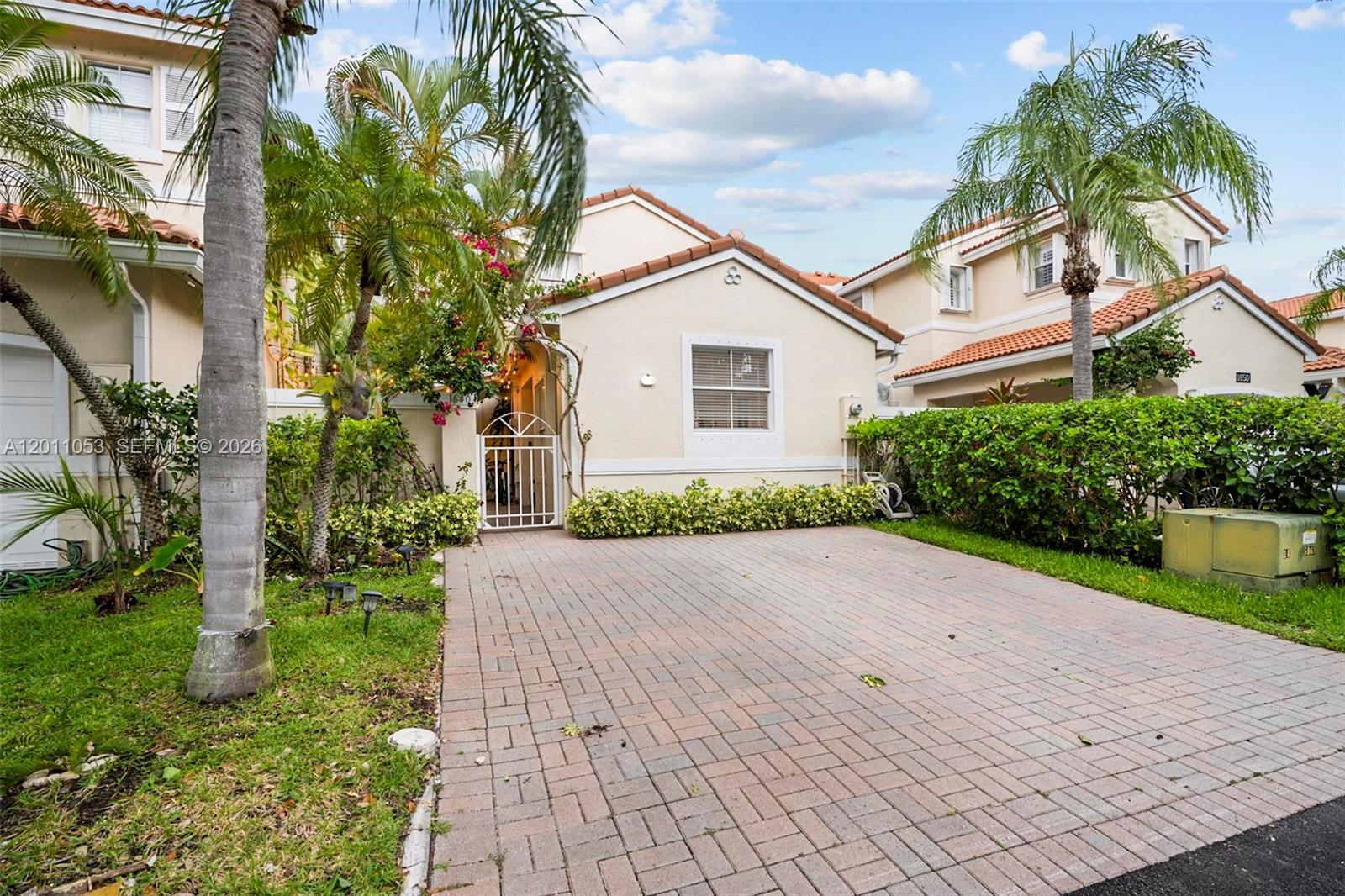 A beige house with a brick driveway, a white gate, and palm trees — 1640 Weeping Willow Way # 1640, Hollywood FL 33019, HOLLYWOOD, FL