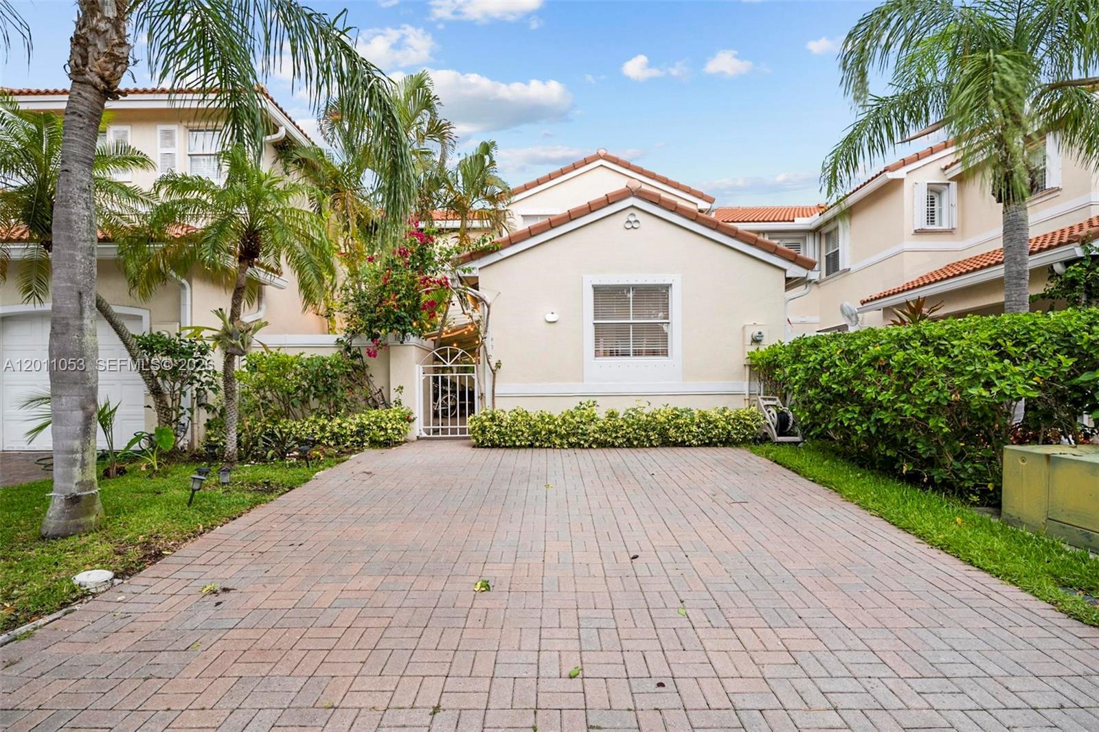 A paved driveway leads to the front entrance of a beige house with palm trees — 1640 Weeping Willow Way # 1640, Hollywood FL 33019, HOLLYWOOD, FL