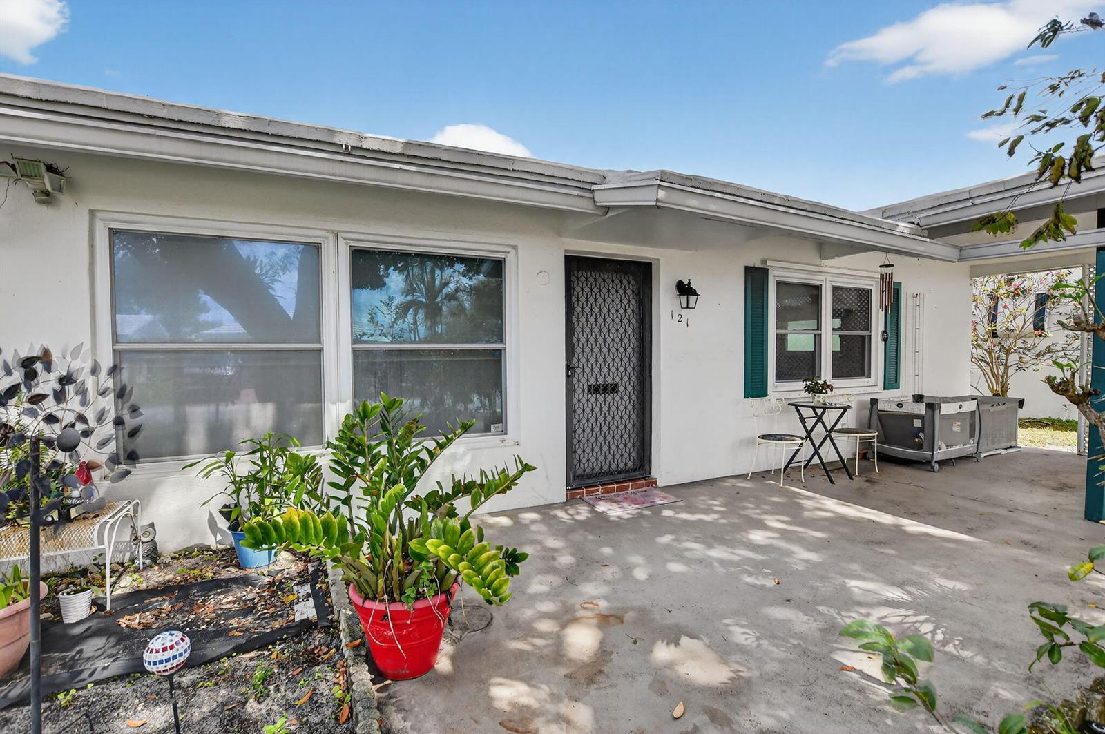 A white one-story house exterior features a concrete patio, green shutters, and a screen door — 121 NW 28th Court, Pompano Beach FL 33064, POMPANO BEACH, FL