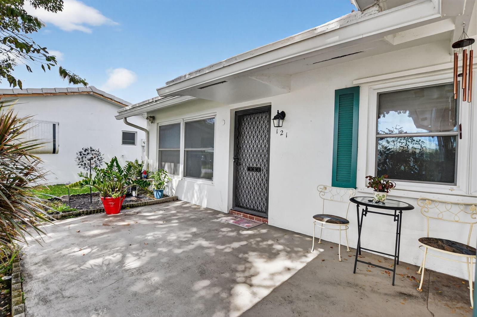 A white house exterior features a concrete patio, a screen door, and teal shutters — 121 NW 28th Court, Pompano Beach FL 33064, POMPANO BEACH, FL