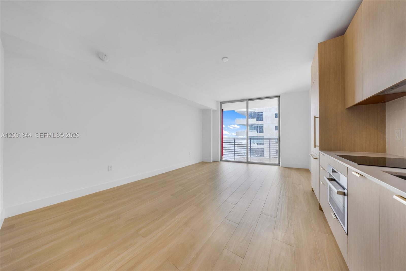 A modern kitchen with light wood cabinetry opens into a living area with balcony access — 90 NE 32 # 1013, Miami FL 33137, MIAMI, FL