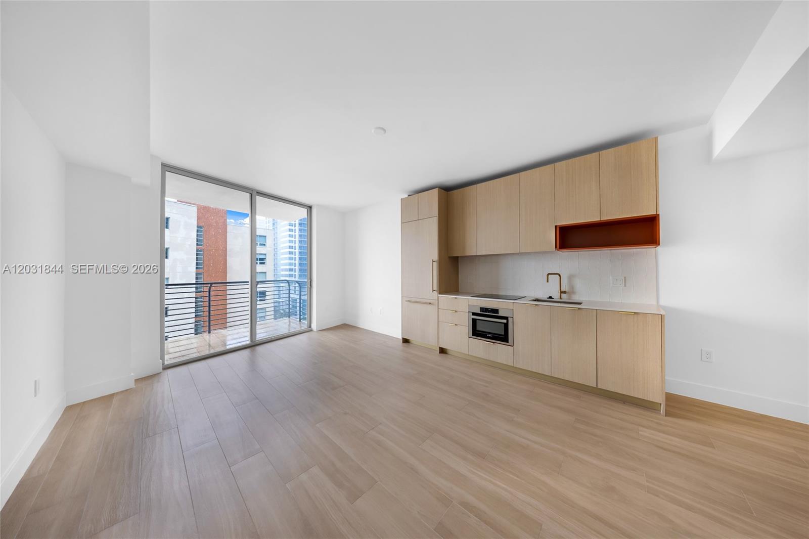 A modern studio apartment features light wood cabinetry, stainless steel appliances, and a private balcony — 90 NE 32 # 1013, Miami FL 33137, MIAMI, FL