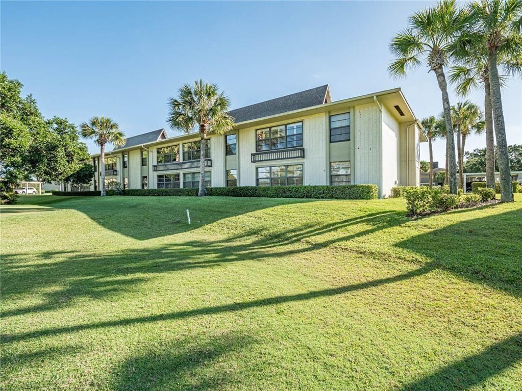 A multi-story apartment building with light-colored siding sits behind a large, grassy lawn — 32 Plantation Drive # 103, Vero Beach FL 32966, VERO BEACH, FL