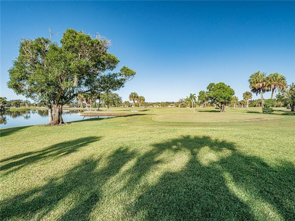 A view of a grassy golf course with a pond, large trees, and palm trees — 32 Plantation Drive # 103, Vero Beach FL 32966, VERO BEACH, FL