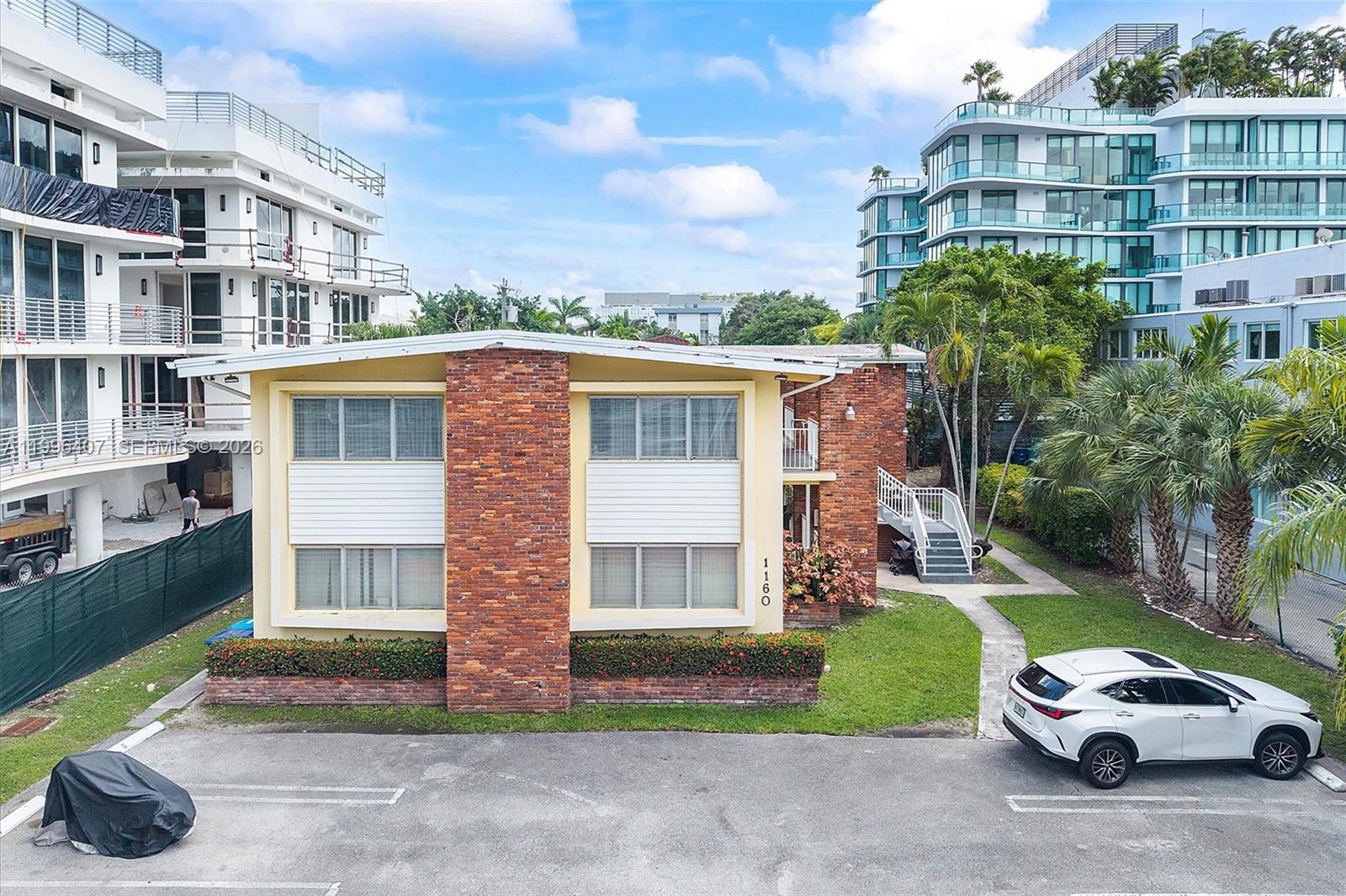 A two-story brick and yellow building sits between modern apartment complexes with a parking lot — 1160 100th St, Bay Harbor Islands FL 33154, BAY HARBOR ISLANDS, FL