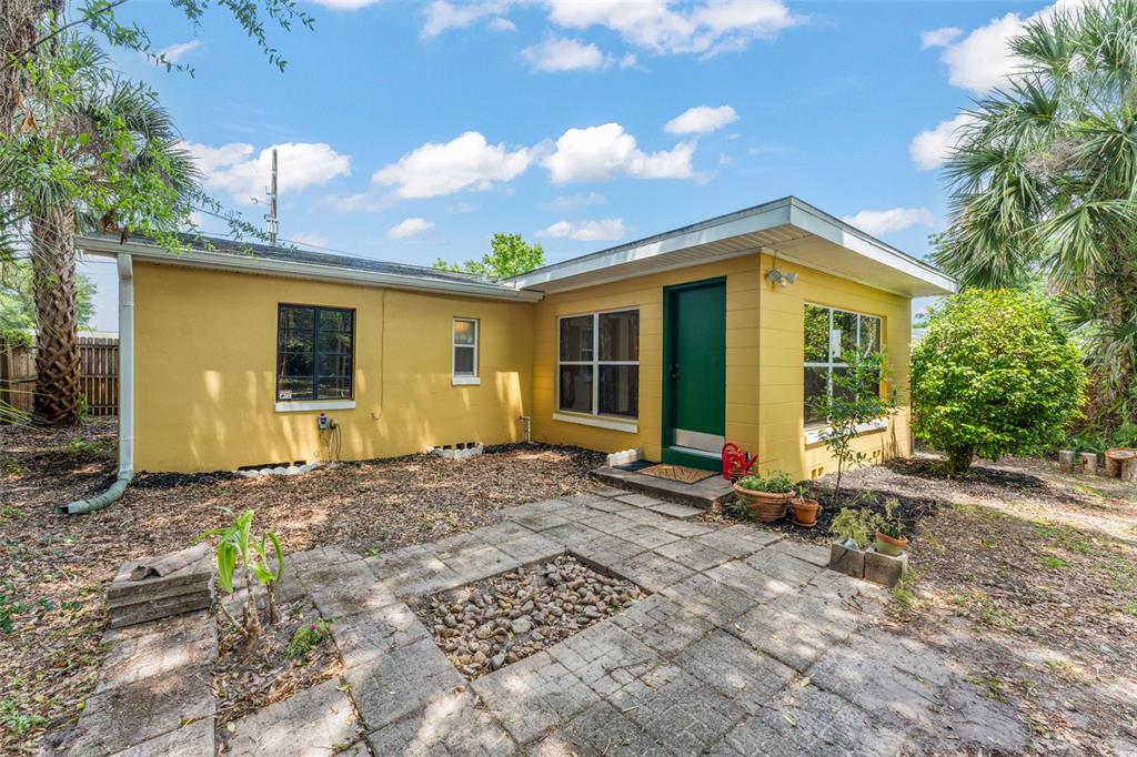 A yellow house exterior features a green door, a stone patio, and surrounding palm trees — 440 CAMBRIDGE BOULEVARD, WINTER PARK, FL