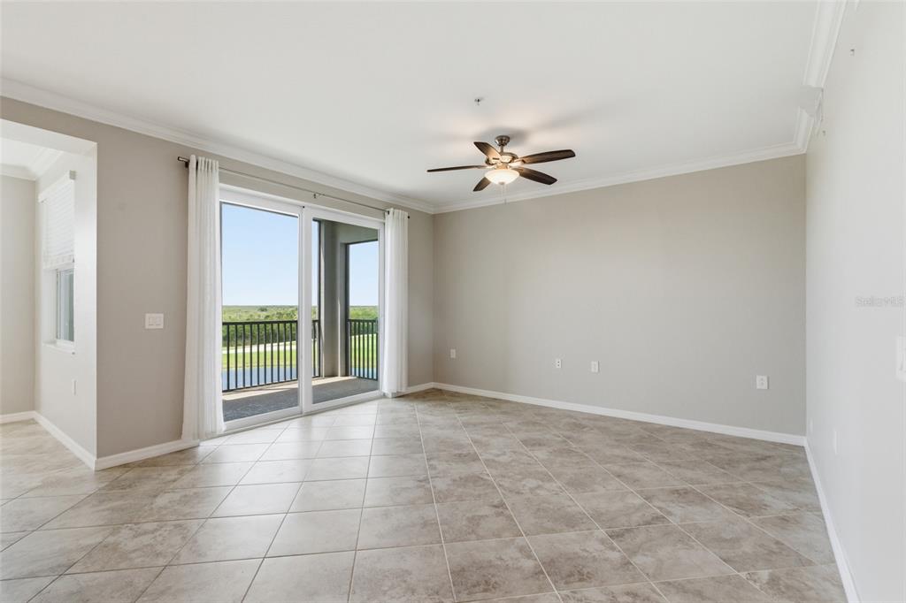 An empty living room features tile flooring, a ceiling fan, and sliding glass doors to a balcony — 14081 HERITAGE LANDING BOULEVARD UNIT 237, PUNTA GORDA, FL