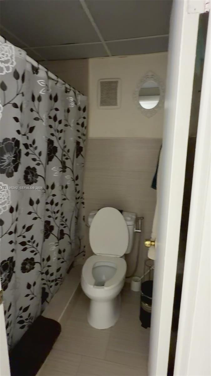 A small bathroom features a white toilet, a floral shower curtain, and light-colored walls — 1225 W 35th St # 2A, Hialeah FL 33012, HIALEAH, FL