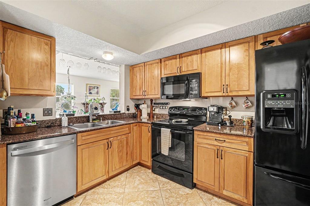 A kitchen features light wood cabinets, granite countertops, a black refrigerator, and stainless steel appliances — 2625 TERRA CEIA BAY BOULEVARD UNIT 201, PALMETTO, FL
