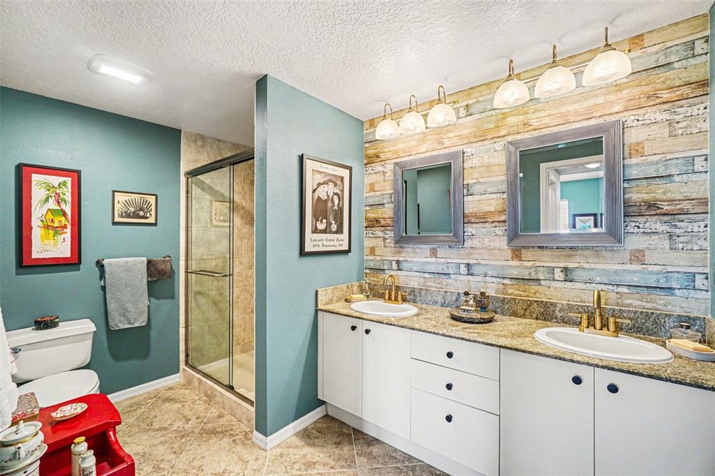 A bathroom features a double vanity with granite countertops, a wood-plank accent wall, and a shower — 2625 TERRA CEIA BAY BOULEVARD UNIT 201, PALMETTO, FL