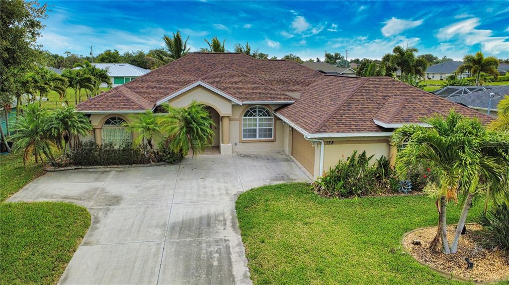 A single-story house with a brown shingled roof, beige stucco walls, and a concrete driveway — 138 BROADMOOR LANE, ROTONDA WEST, FL