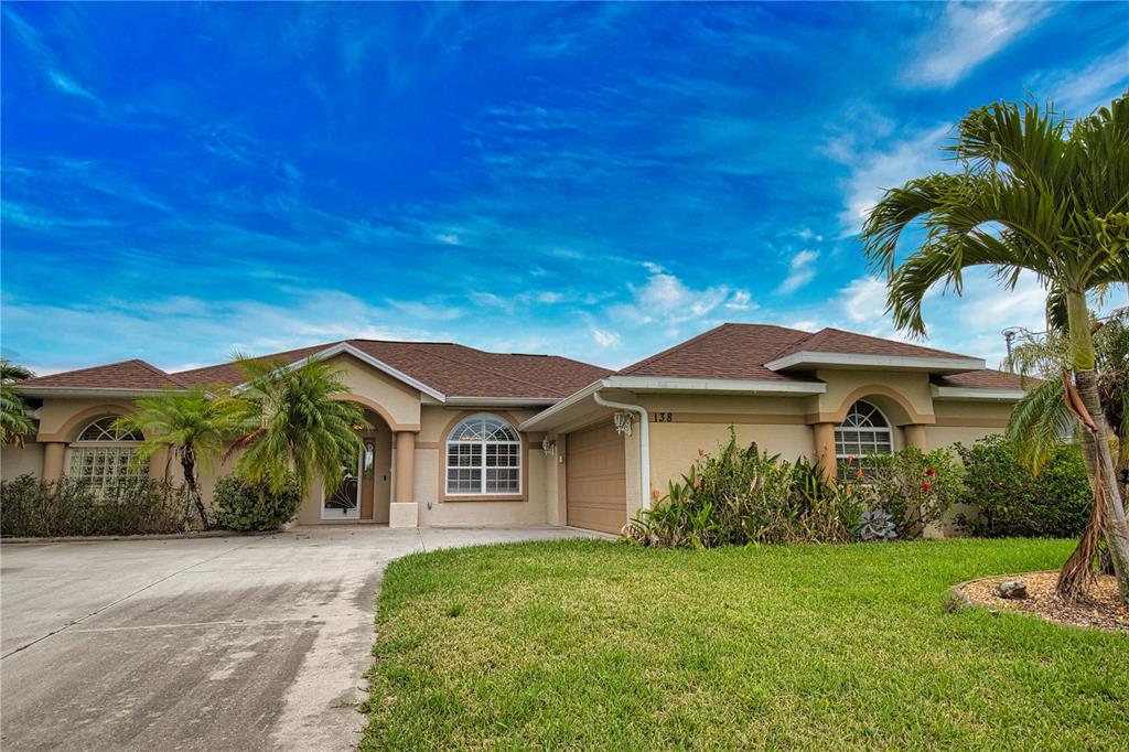 A single-story suburban house with a tan stucco exterior, a brown roof, and a palm tree — 138 BROADMOOR LANE, ROTONDA WEST, FL