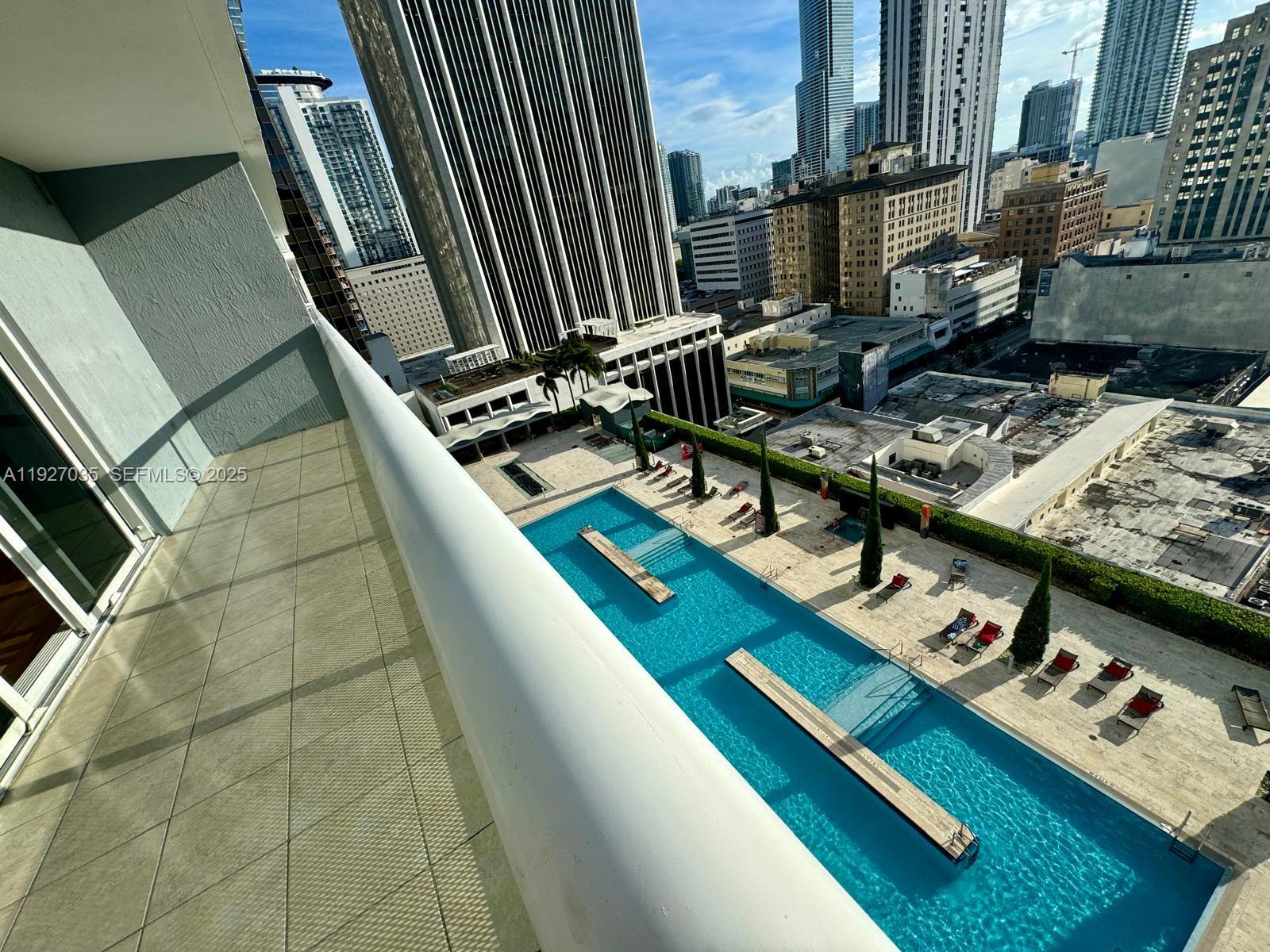 A high-angle view from a balcony overlooking a rectangular swimming pool and city skyline — 50 BISCAYNE BLVD # 1703, Miami FL 33132, MIAMI, FL