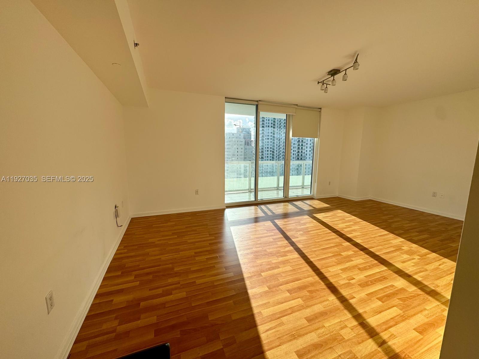 An empty room features wood-look flooring, white walls, a ceiling light fixture, and a balcony — 50 BISCAYNE BLVD # 1703, Miami FL 33132, MIAMI, FL